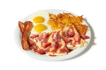 Denny’s Berry Vanilla Crepe Breakfast with crepes topped with strawberries, vanilla cream, and served with eggs, bacon, and hash browns.