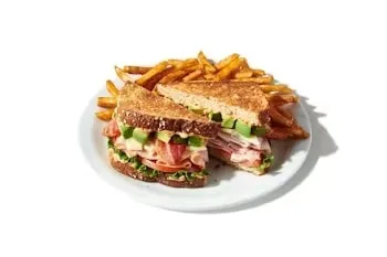 Denny’s Cali Club Sandwich layered with turkey, bacon, lettuce, tomato, and avocado on toasted bread.