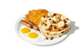 Denny’s Choconana Pancake Slam with chocolate chip pancakes topped with banana slices, served with eggs, bacon, and hash browns.