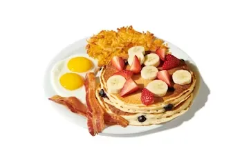 Denny’s Double Berry Pancake Slam with pancakes topped with strawberries and blueberries, served with eggs, bacon, and hash browns.