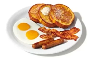 Denny’s French Toast Slam with golden French toast, eggs, bacon, and sausage links on a plate.