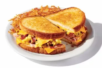 Denny’s Grand Slamwich breakfast sandwich with eggs, bacon, sausage, melted cheese, and golden hash browns on the side.