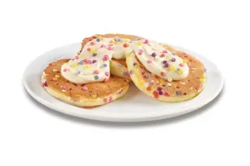 Denny’s Kid’s Birthday Pancakes with colorful sprinkles, whipped cream, and icing drizzle.