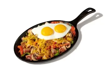 Denny’s Santa Fe Skillet with scrambled eggs, peppers, onions, and seasoned potatoes in a black skillet pan.
